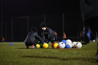 Kinder sortieren bunte Bälle während eines Abendtrainings auf einem Fußballplatz.