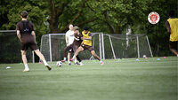 Zwei Fußballspieler im Training im Zweikampf um den Ball, daneben weitere Spieler, Hütchen und kleine Tore; oben rechts das FC‑St.-Pauli‑Logo.