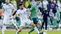 Zwei Fußballspieler kämpfen um den Ball auf einem Rasenplatz.