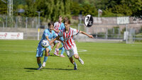 Jugendspieler vom SC Freiburg im Zweikampf mit Gegner auf dem Fußballfeld, Ball im Spiel, Vereinslogo sichtbar.