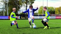 Drei junge Fußballspieler trainieren auf einem Kunstrasenplatz mit Ball.