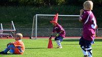 Kinder beim Fußballtraining spielen mit Hütchen auf dem Rasenplatz vor einem Tor.