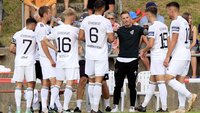 Spieler einer Fußballmannschaft in weißen Trikots stehen während einer Pause zusammen und sprechen mit einem Trainer.