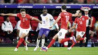 Österreichische Spieler im roten Trikot verteidigen gegen einen französischen Spieler im weißen Trikot während eines Fußballspiels.