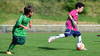 Ein junger Torspieler dribbelt während des Fußballtrainings auf dem Rasenplatz, verfolgt von einem Mitspieler.