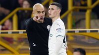 Ein Trainer in schwarzer Kleidung mit Manchester City-Logo gestikuliert energisch neben einem Spieler im weißen Trikot.