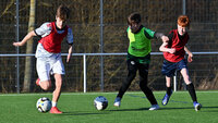 Drei Jugendfußballer beim Training auf einem Kunstrasenplatz in einem intensiven Zweikampf um den Ball.