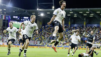 Jubelnde Fußballmannschaft: Spieler Nr. 8 springt hoch und feiert, Mitspieler und Bank jubeln im Stadion.