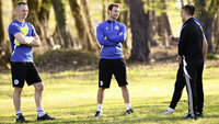 Drei Fußballtrainer im blauen Trainingsoutfit unterhalten sich auf dem Sportplatz am Spielfeldrand im Grünen.