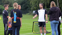 Trainer erklärt Eltern und Kindern Trainingsablauf auf dem Fußballplatz mit Hütchen und Minitoren.